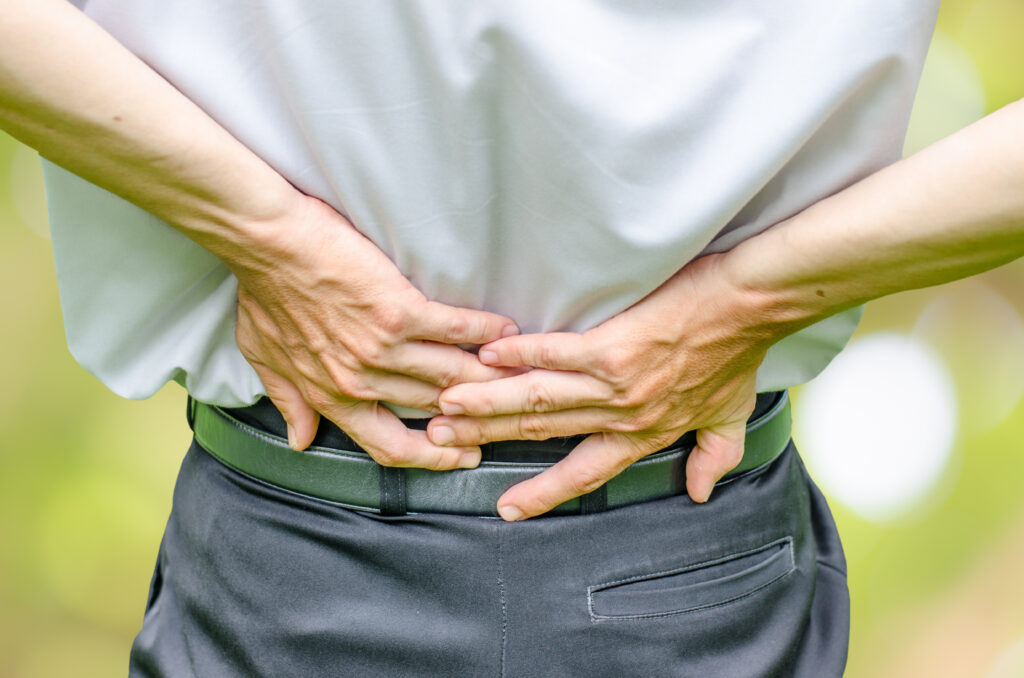 close up of a man holding his back in pain, isolated on white background, monochrome photo with red as a symbol for the hardening