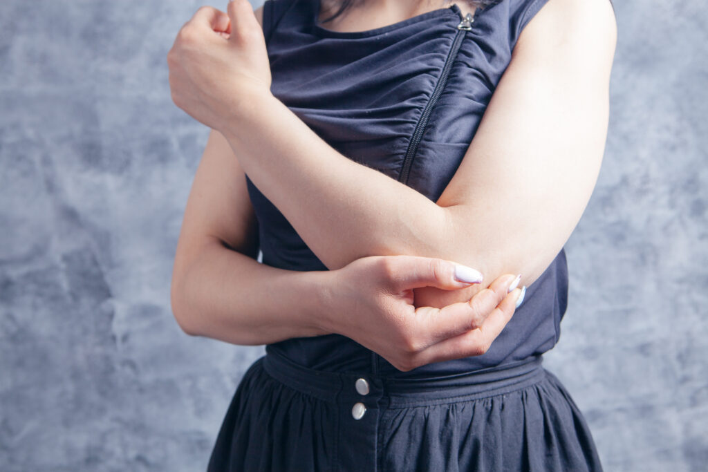 young woman has a sore elbow on gray background